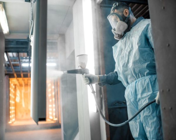 Painter in protective wear paints metal products with powder paint. Powder coating process at the manufacturing. High quality photo